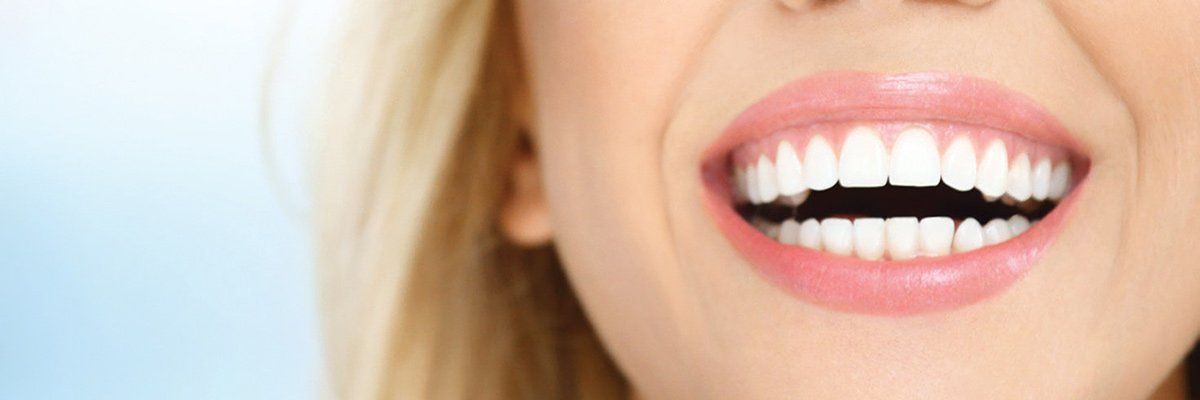 A close up of a woman 's mouth with white teeth and pink lips.