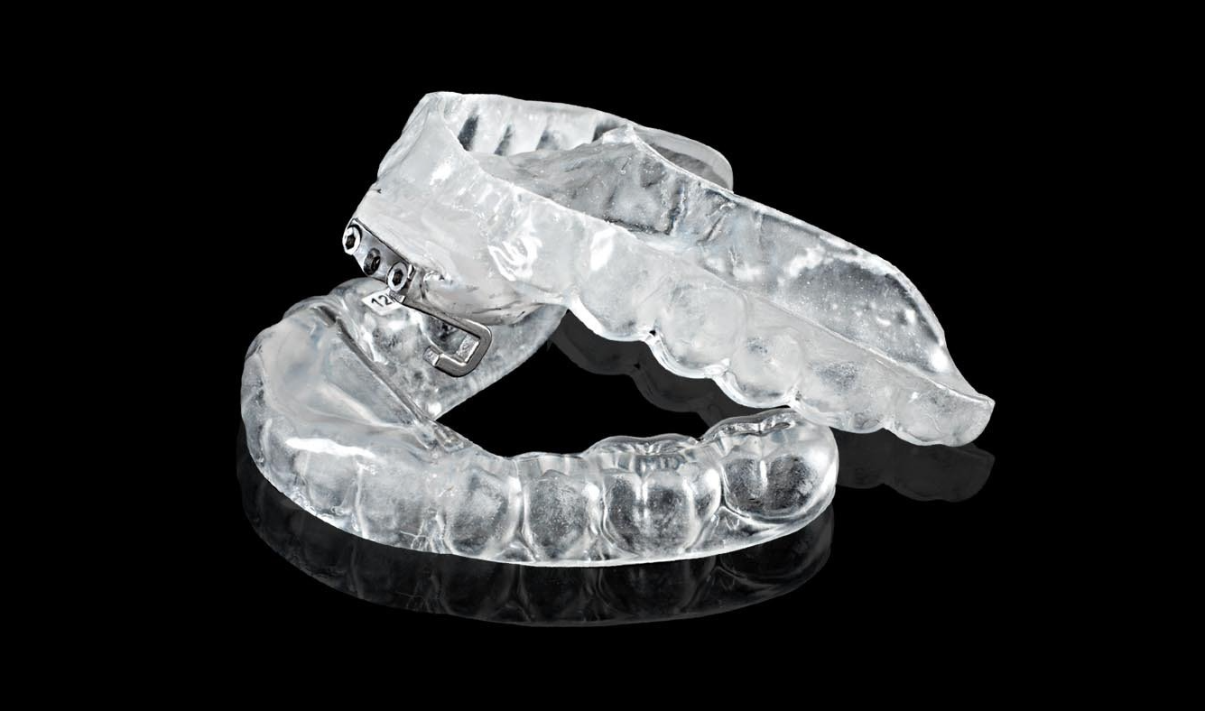 A pair of clear plastic mouth guards on a black surface.