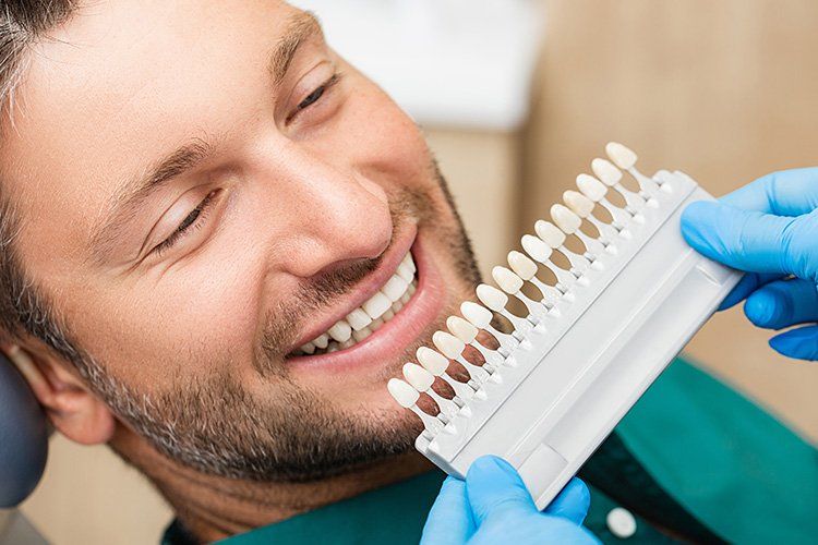 A man is sitting in a dental chair looking at a tooth color chart.