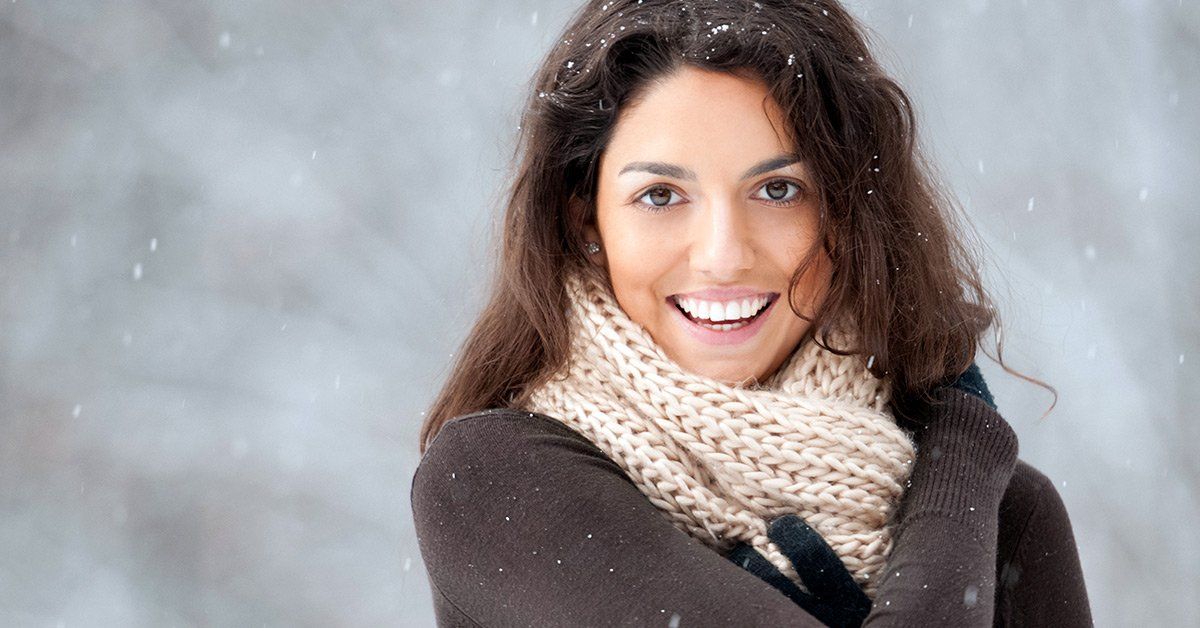 A woman wearing a scarf and a sweater is smiling in the snow.