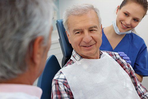 An older man is sitting in a dental chair talking to a nurse.