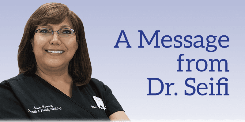 A woman wearing glasses is smiling in front of a sign that says a message from dr. seifi