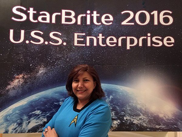 A woman stands in front of a sign that says starbrite 2016 u.s.s. enterprise