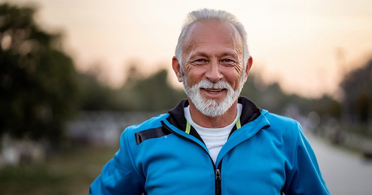 An older man with a beard is wearing a blue jacket and smiling.