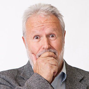 An older man with a beard is covering his mouth with his hand.