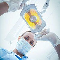 A female dentist wearing a mask and gloves is operating on a patient.