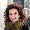 A woman with curly hair is wearing a scarf around her neck and smiling.