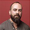 A man with a beard is standing in front of a red background.
