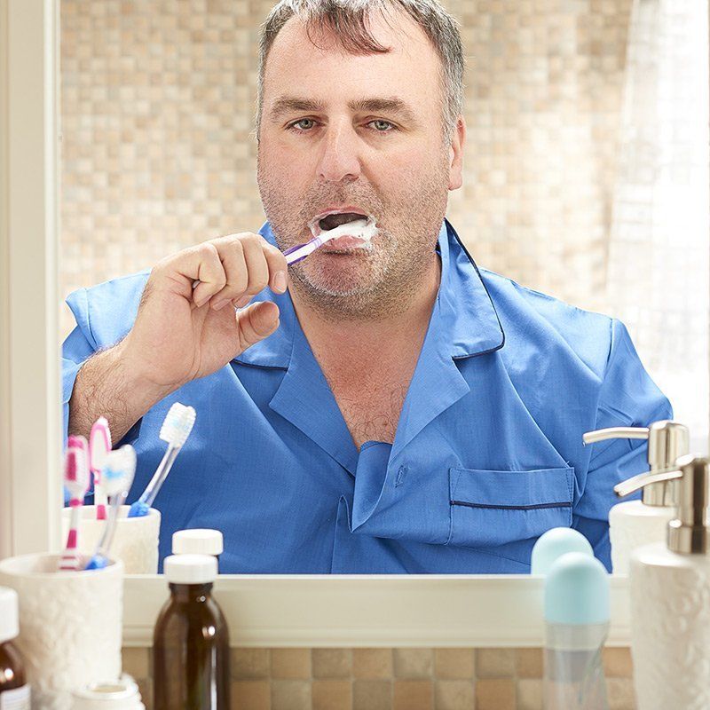 A man in a blue shirt is brushing his teeth in front of a mirror