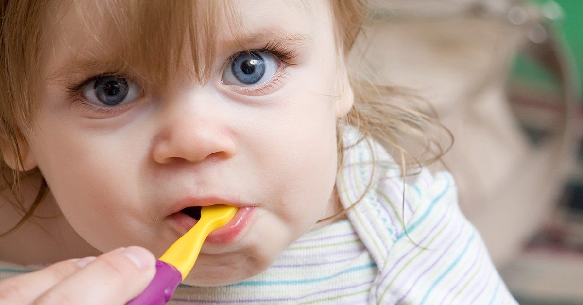 A little girl is brushing her teeth with a yellow toothbrush.