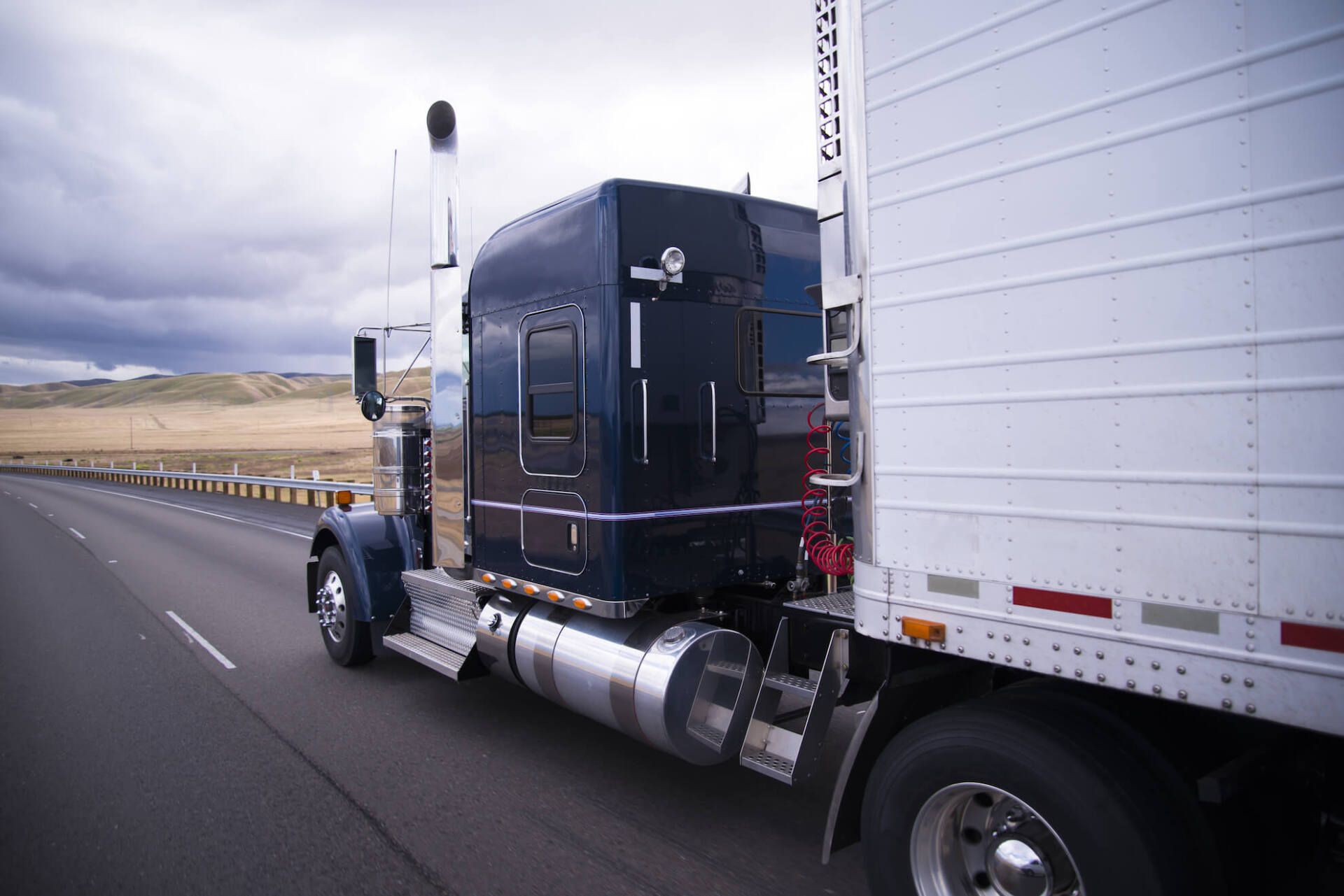 A semi truck is driving down a highway next to a white trailer.