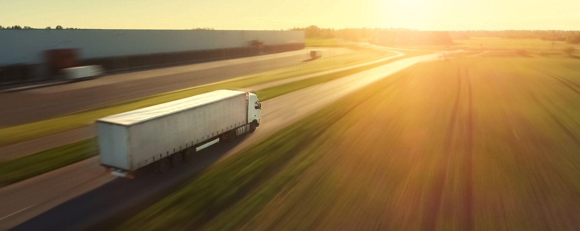 An aerial view of a semi truck driving down a highway at sunset.