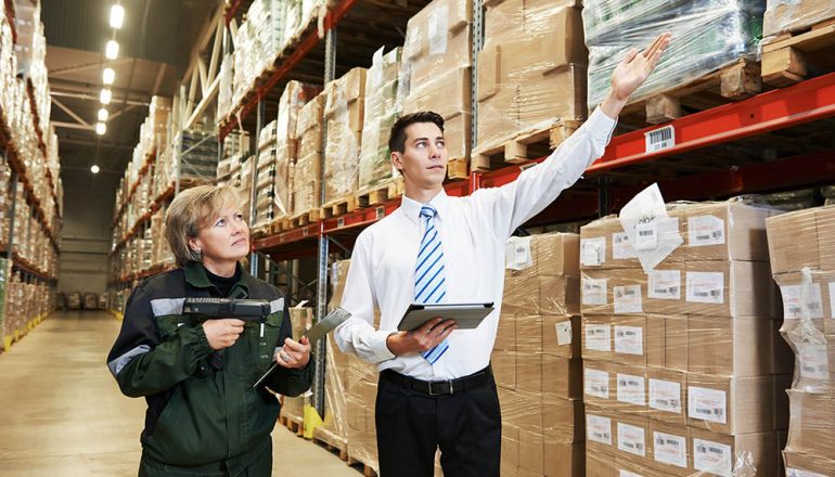 Man in warehouse pointing at shelves; woman scans barcode reader.