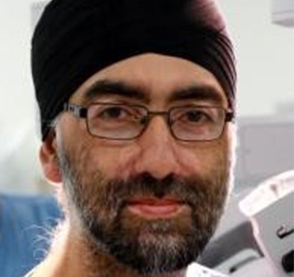 Close-up of a man wearing glasses and a black turban, with a beard and a slight smile.