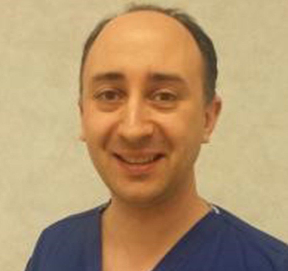 Smiling person in blue scrubs against a beige background
