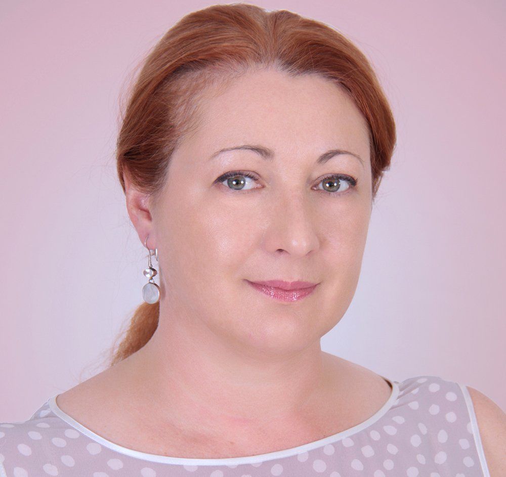 Portrait of a woman with red hair in a light pink top against a pale pink background