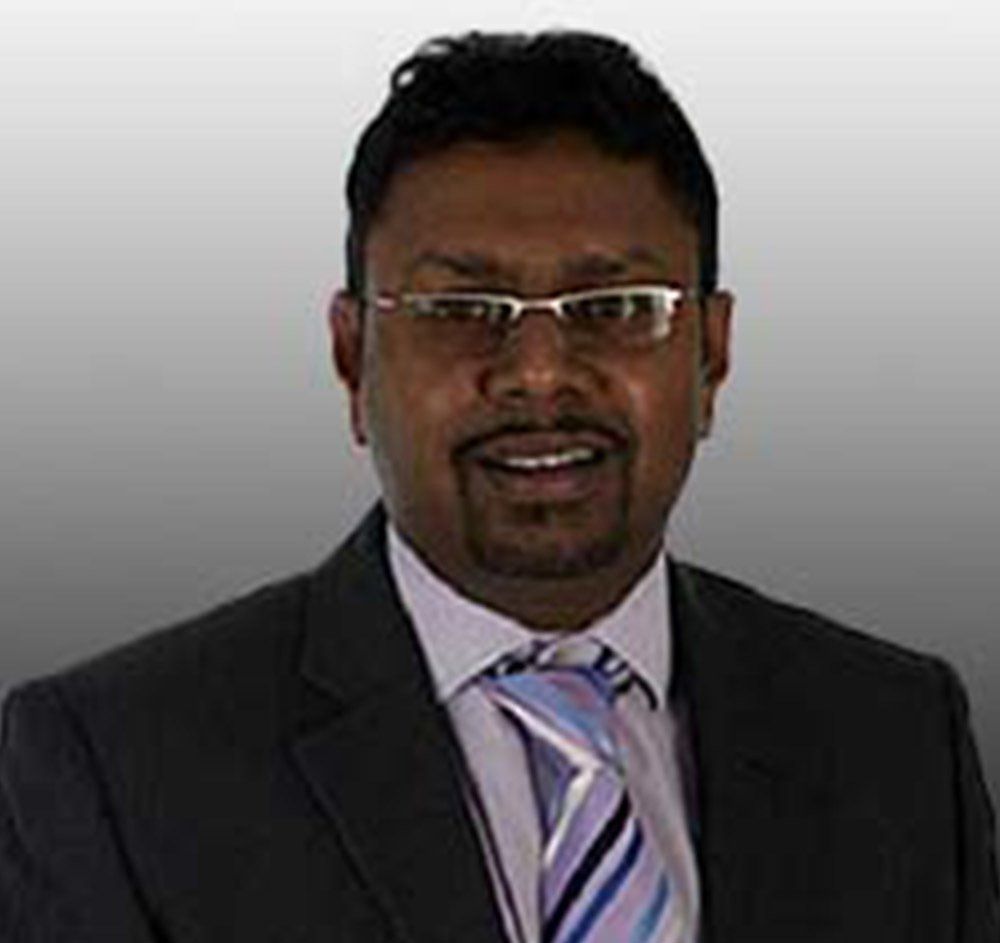 Man in a dark suit and striped tie, wearing glasses, against a light gray background