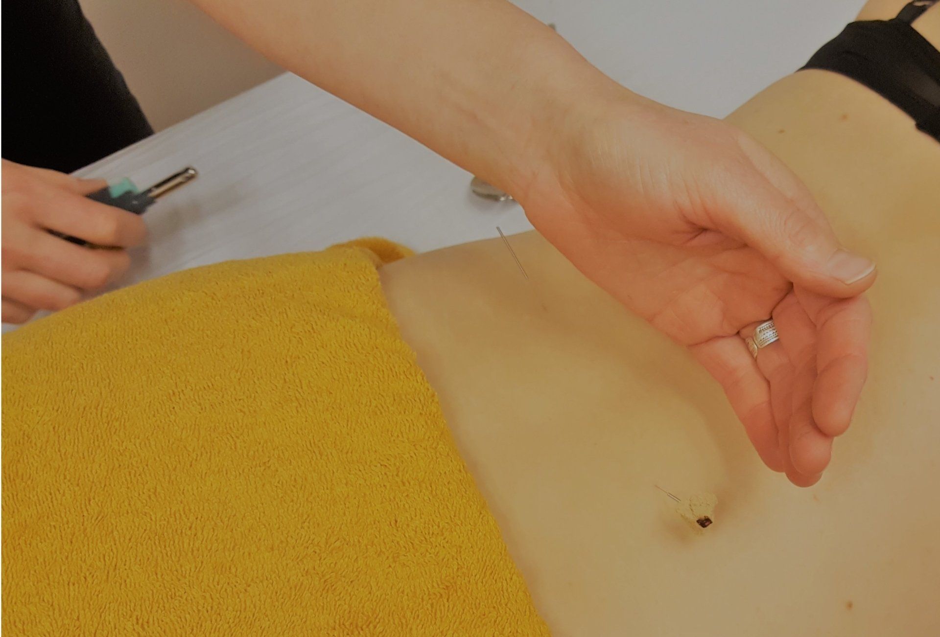 Tijdens een massage of behandeling voelt de hand op de buik van een persoon, naast een gele handdoek.