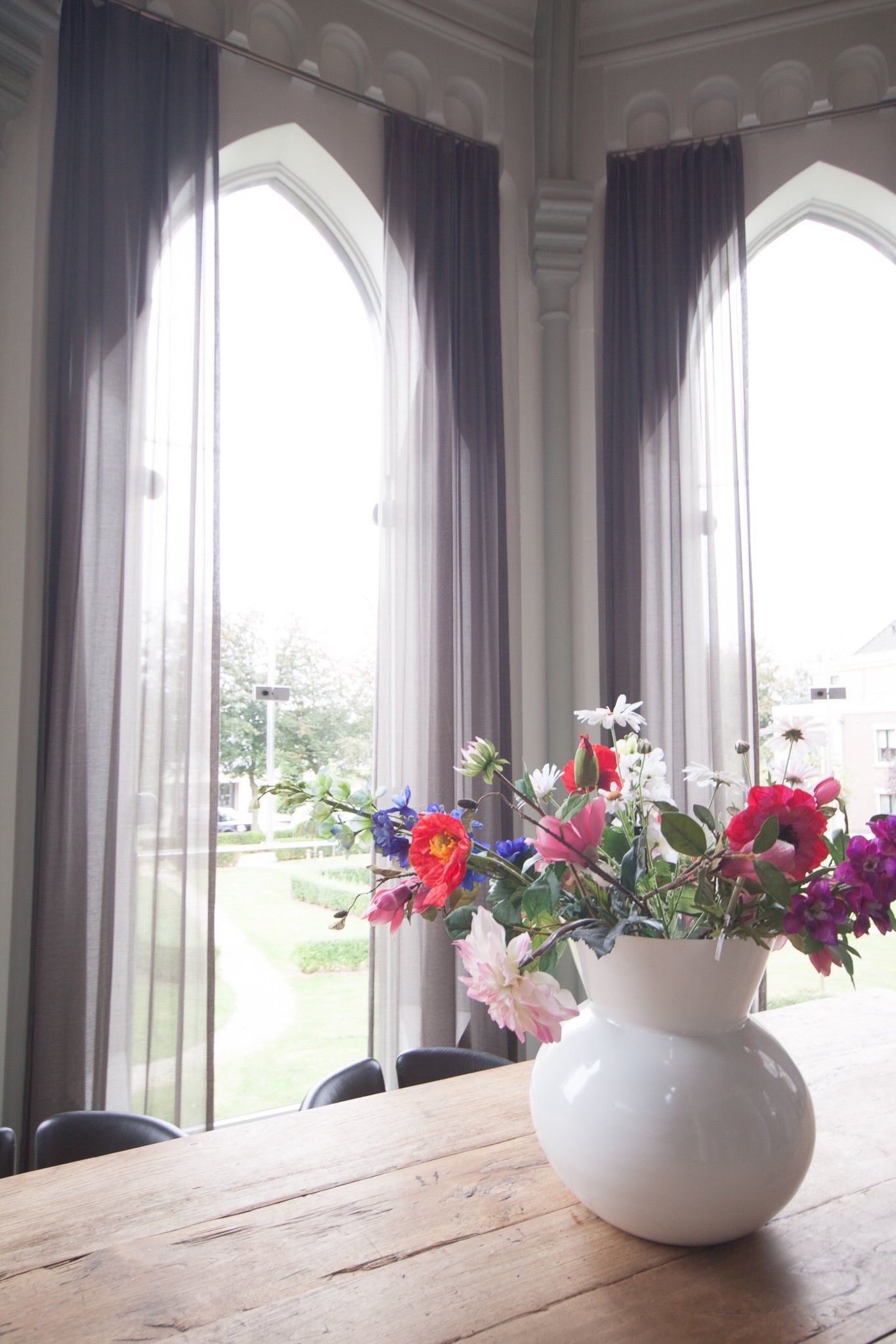 Een vaas met bloemen staat op een houten tafel voor een raam.