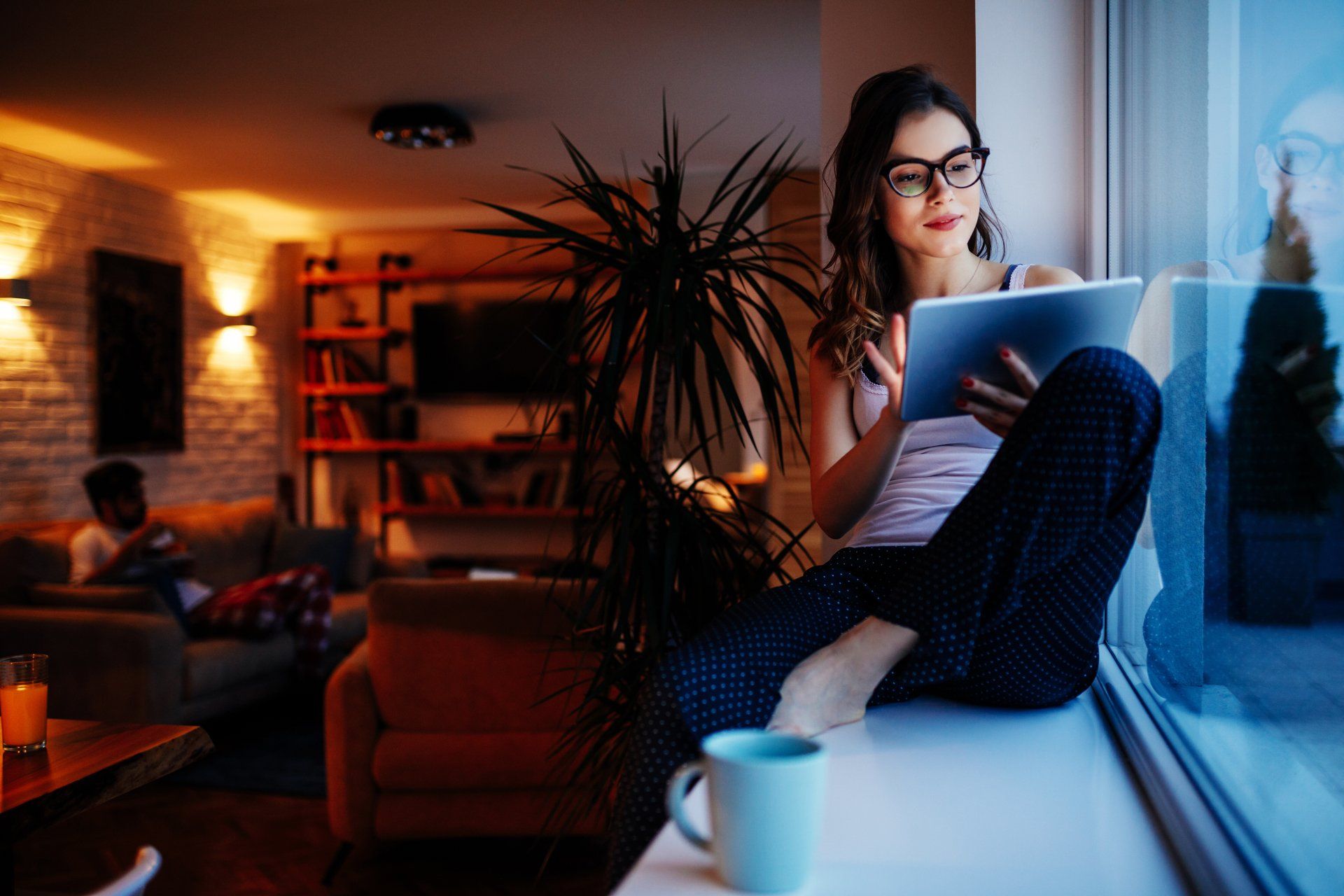 Photo of a young woman sitting by the window and using digital tablet at home.