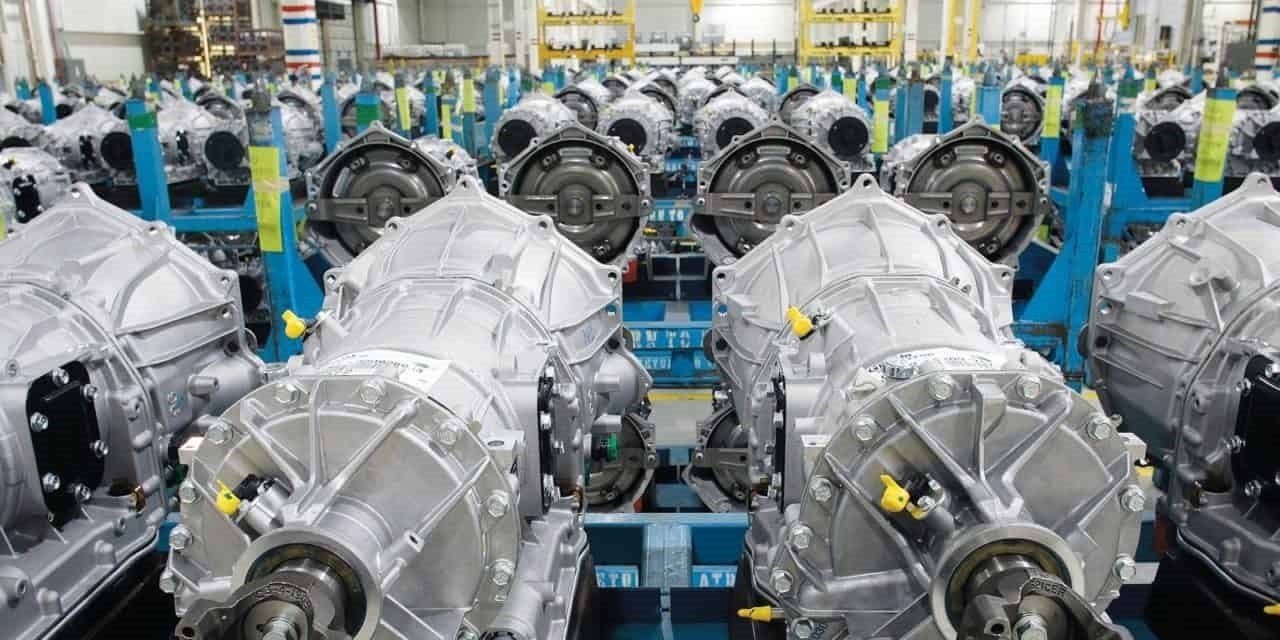 Chaîne d'assemblage de pièces métalliques, vraisemblablement des composants automobiles. Rangées d'objets similaires sur des racks bleus.