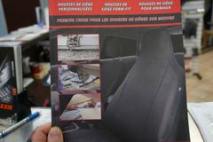 Brochure avec housse de siège auto noire, expliquant l'installation et la protection. Main dans la main dans un magasin.