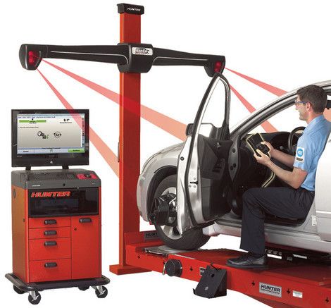 alignement de roues Un mécanicien utilise une machine d'alignement Hunter rouge pour vérifier l'alignement des roues d'une voiture argentée.