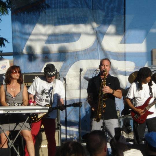 A man playing a saxophone is wearing a shirt that says cat on it