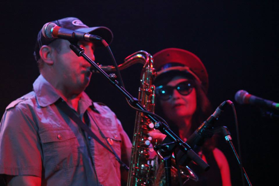 A man is singing into a microphone while a woman plays a saxophone.