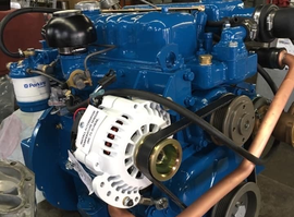 Blue marine diesel engine with white alternator, belts, and copper tubing.
