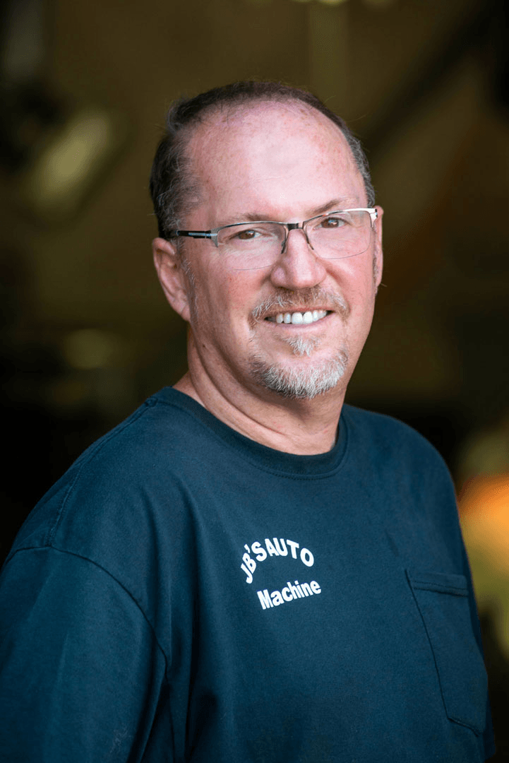 Man with glasses smiling, wearing a navy shirt that says 