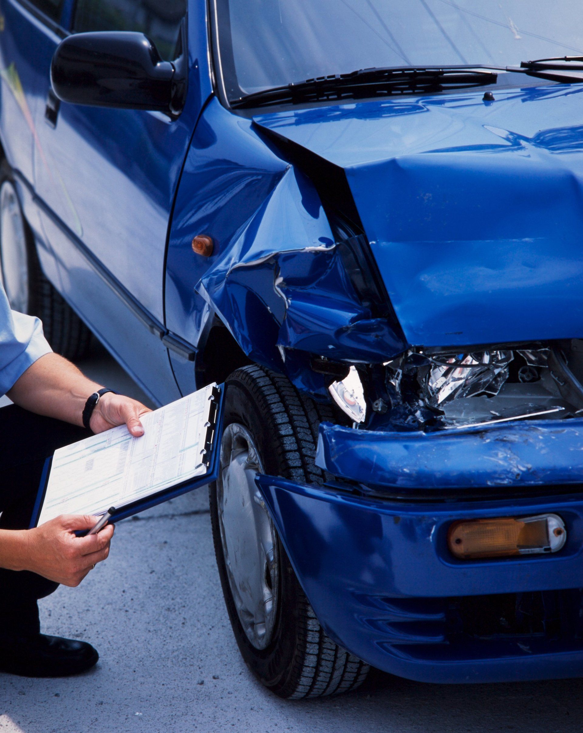 Person inspecting damage to a blue car after a collision.