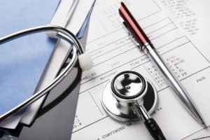 Stethoscope and pen on medical documents in a folder.