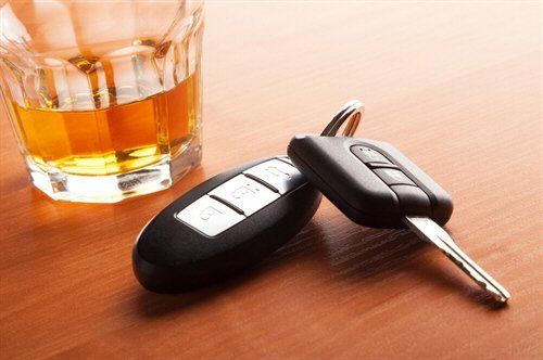 Glass of amber liquor and car keys on a wooden surface.