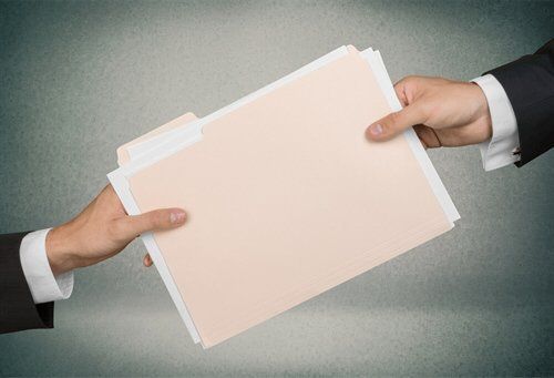 Two people passing a tan file folder, with papers inside, against a gray background.