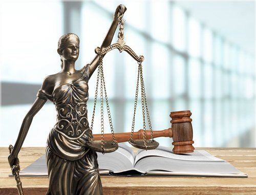 Statue of Lady Justice holding scales, with gavel and open law book on a wooden surface.
