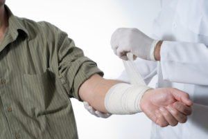 Person in green shirt has arm wrapped in bandage by person in lab coat and gloves.