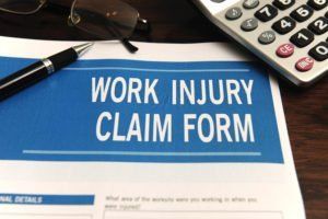 Work injury claim form with pen, glasses, and calculator on desk.