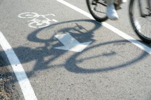 Bicyclist riding on a bike path, casting a shadow over a painted bike symbol and directional arrow.