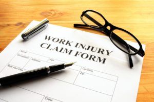 Work injury claim form with pen and glasses on a wooden surface.