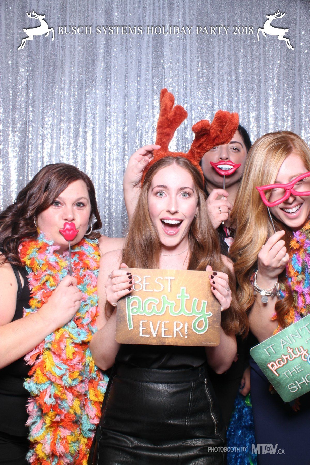 Four people in a photo booth, holding props. One holds a 