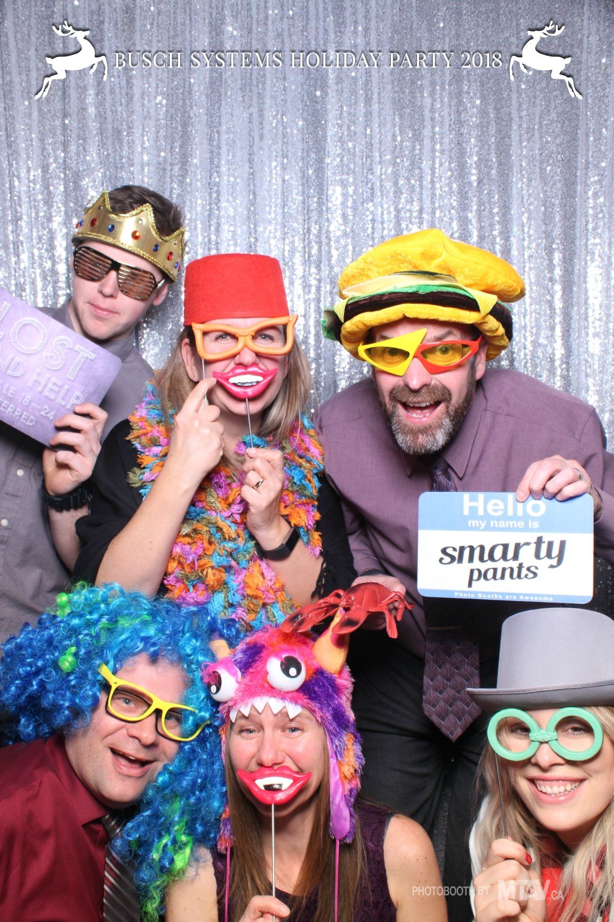 People in photo booth with props; wigs, glasses, a crown, and a 