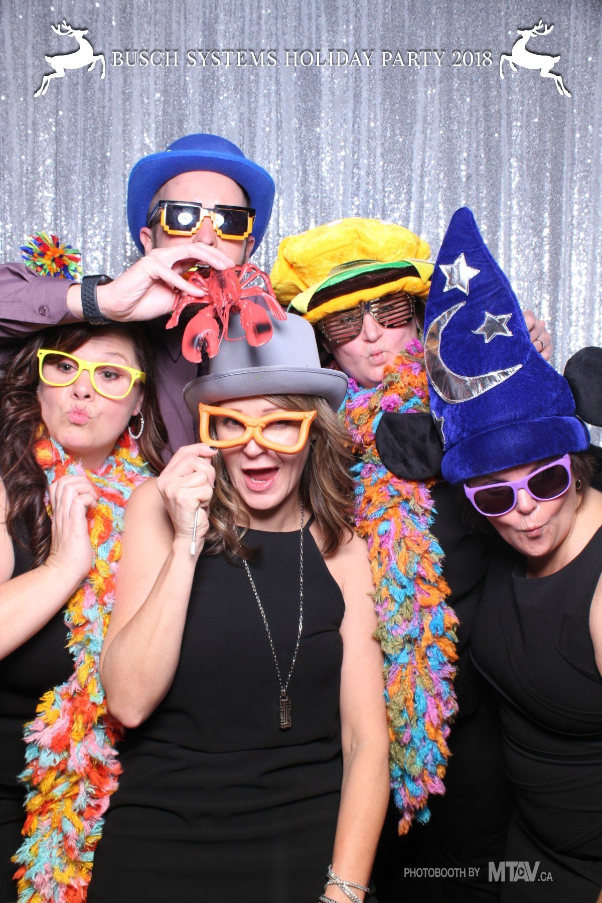 Five people in silly hats and glasses, posing in front of a sparkly backdrop, with various expressions.
