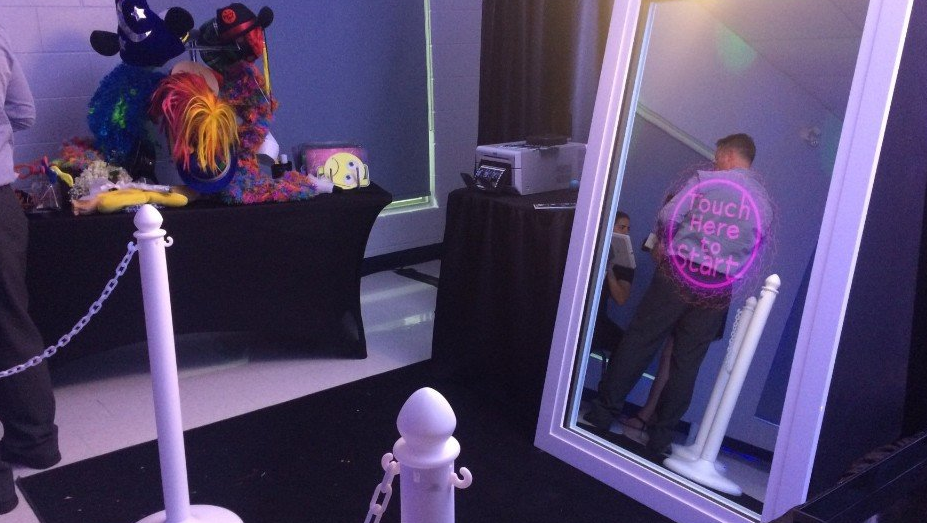 Person reflected in a large mirror with a pink outline, near props and a velvet rope.