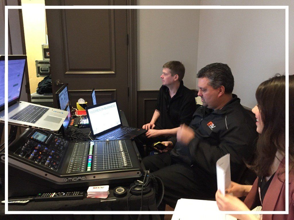 Three people at a sound mixing console. One operates it, two others look at laptops, indoors.