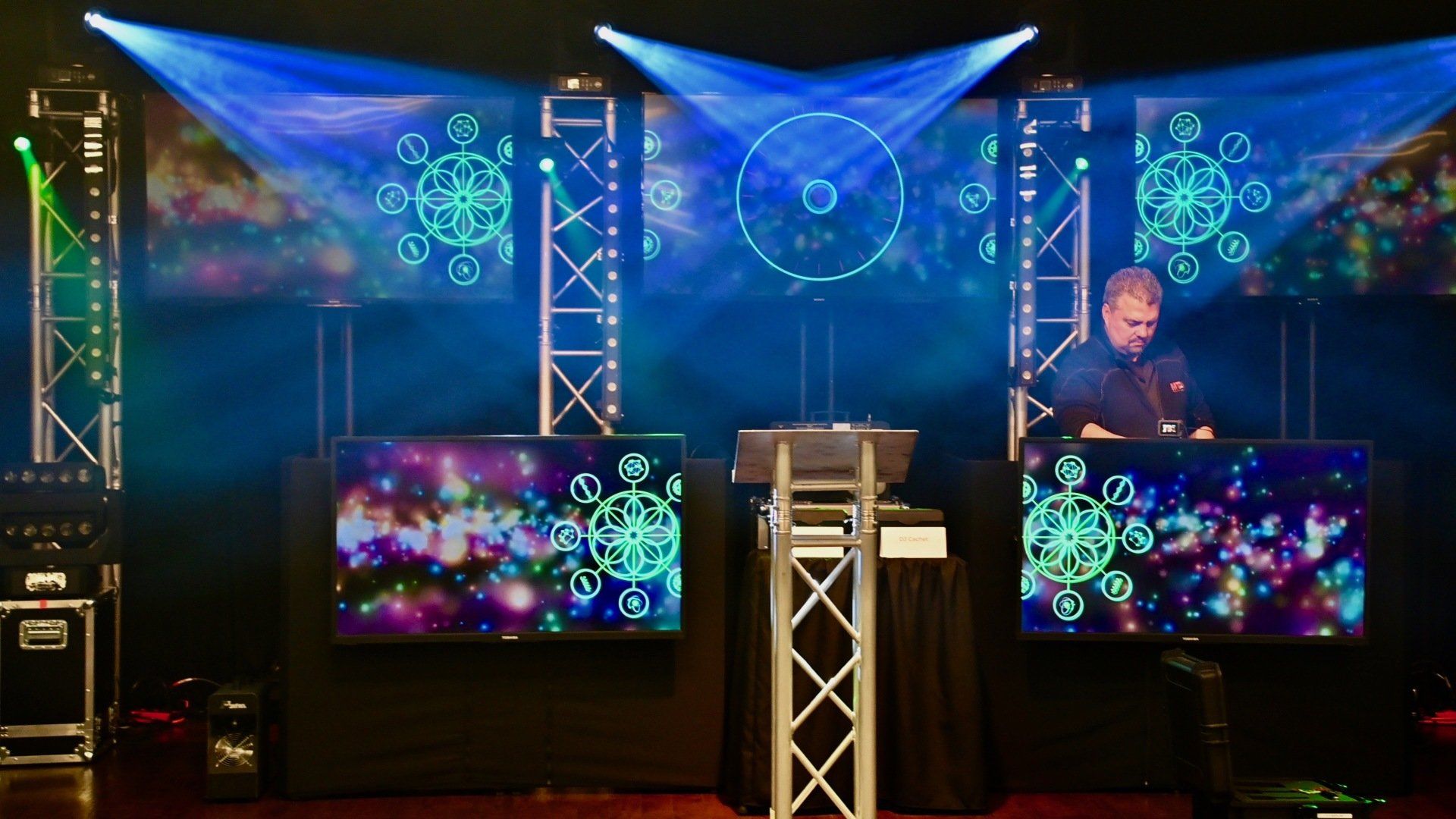 DJ performing on stage with colorful light displays and equipment.