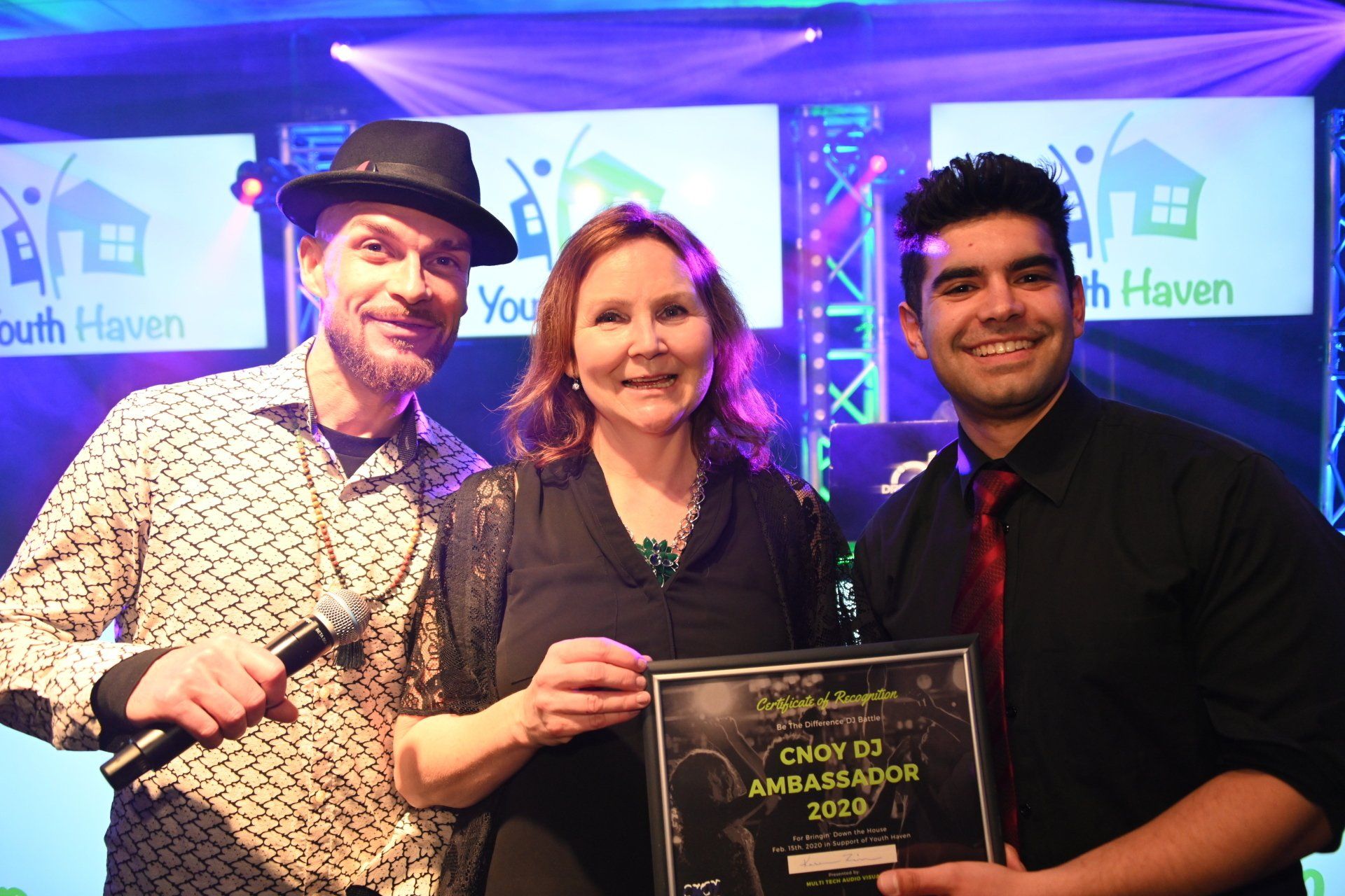 Three people holding an award on a stage with a 