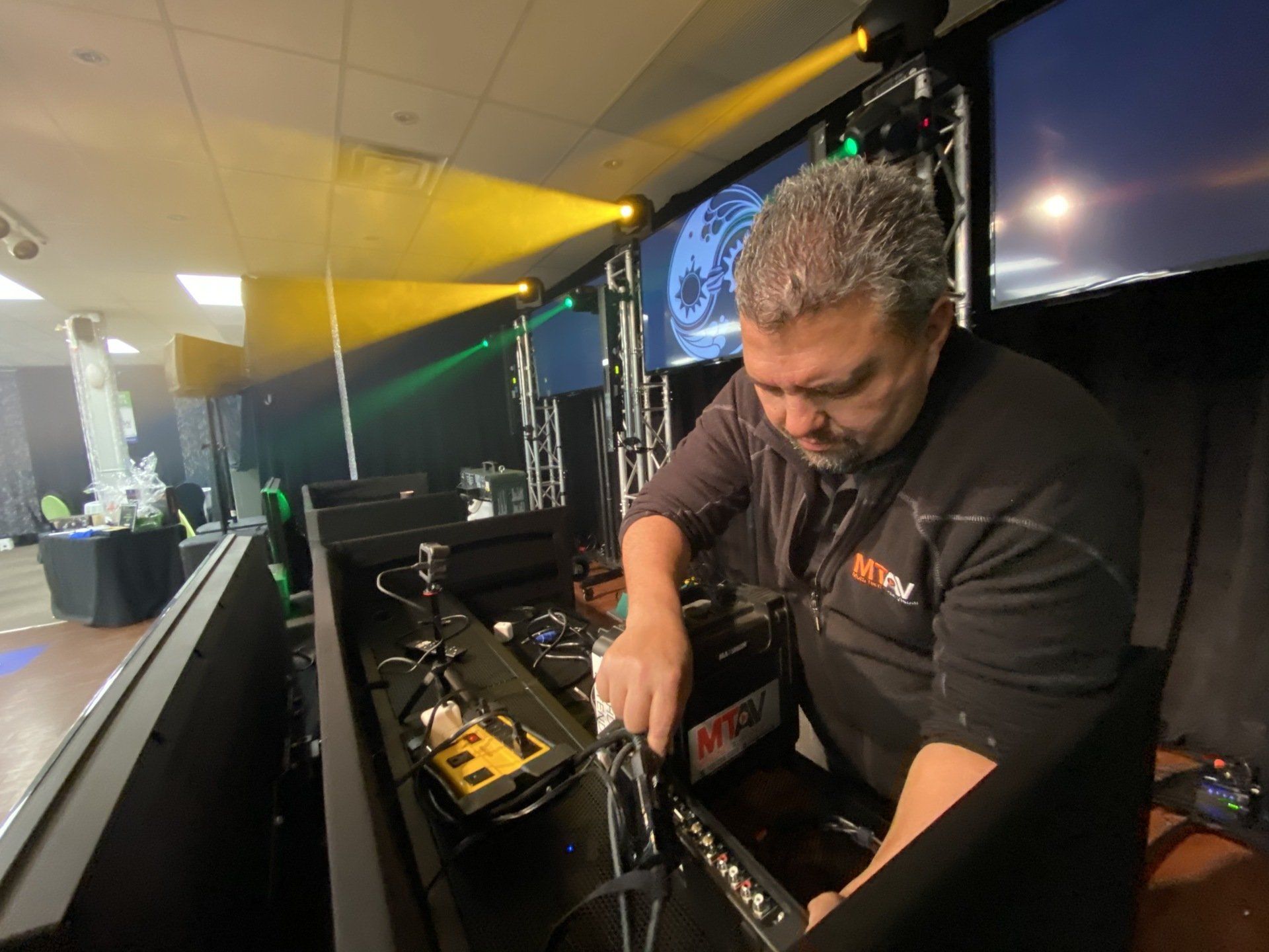 Man setting up equipment at a stage, with lights and screens in the background.