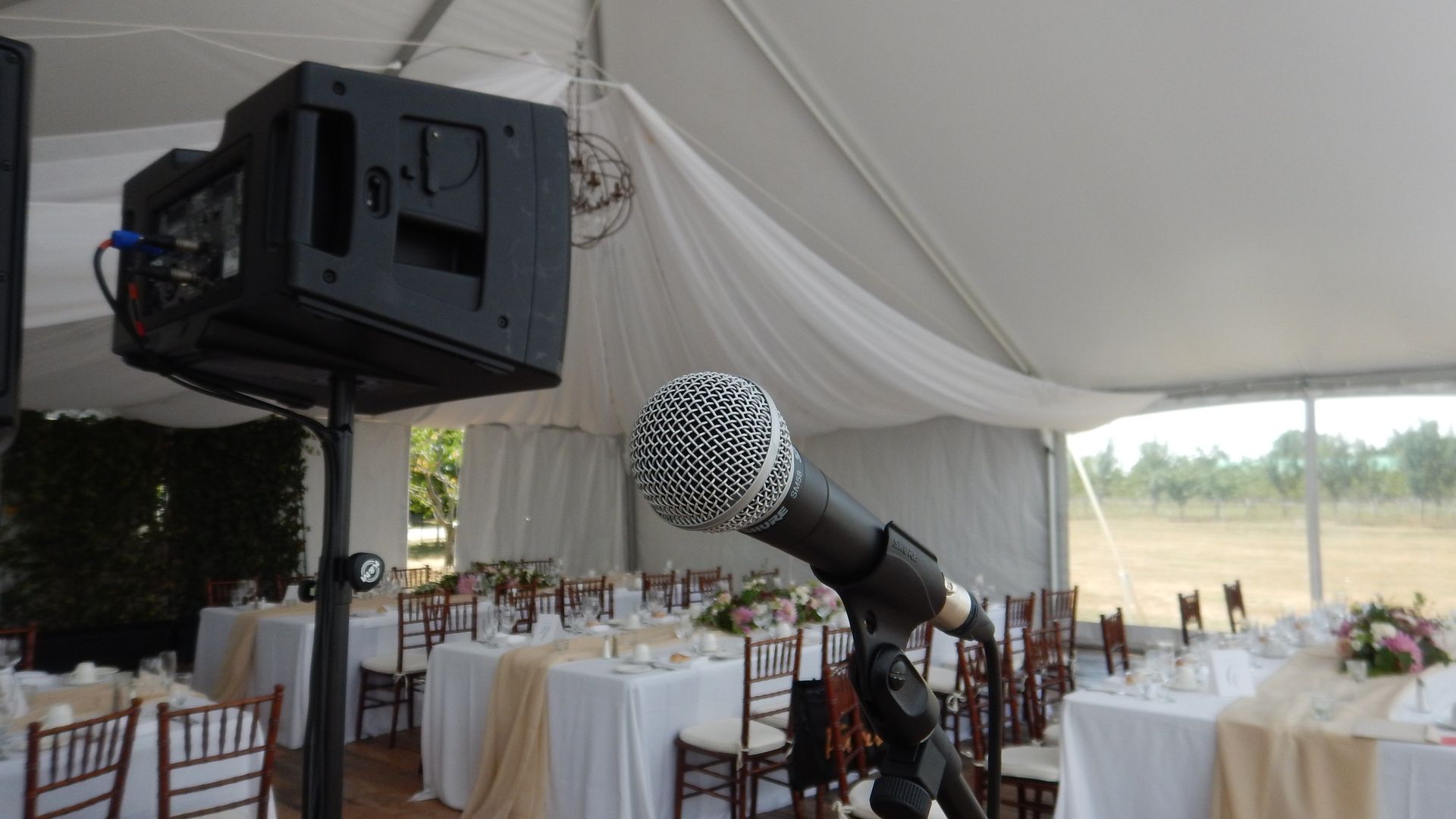 Microphone and speaker set up at a wedding reception inside a white tent; tables and chairs set for guests.