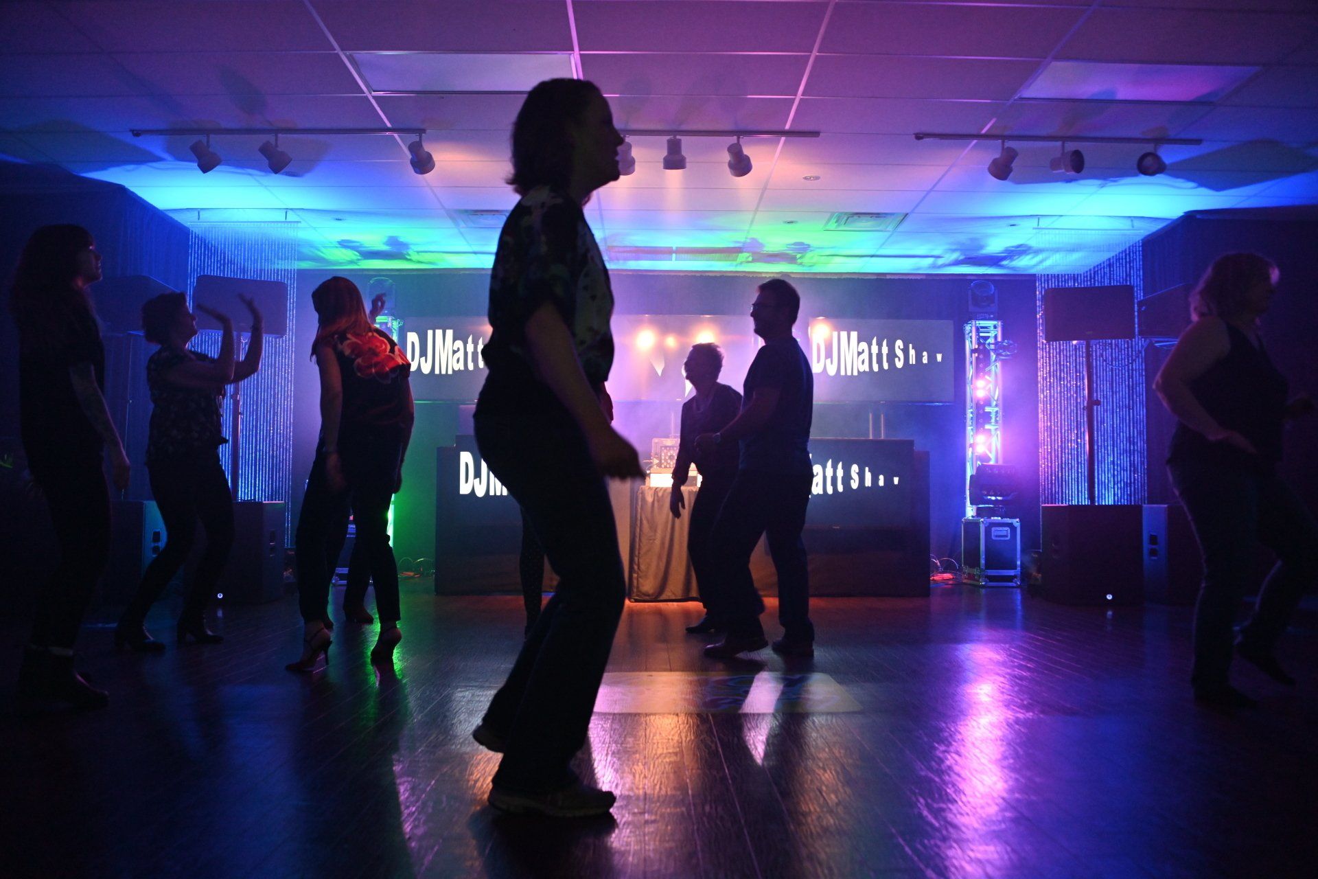 People dancing in a club with colorful lights and a DJ setup.